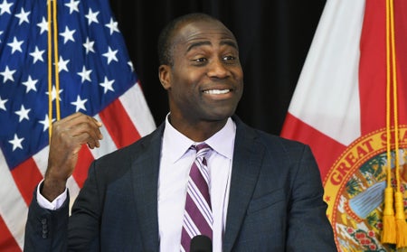 Florida Surgeon General Dr. Joseph Ladapo speaks at a press conference in front of flags.