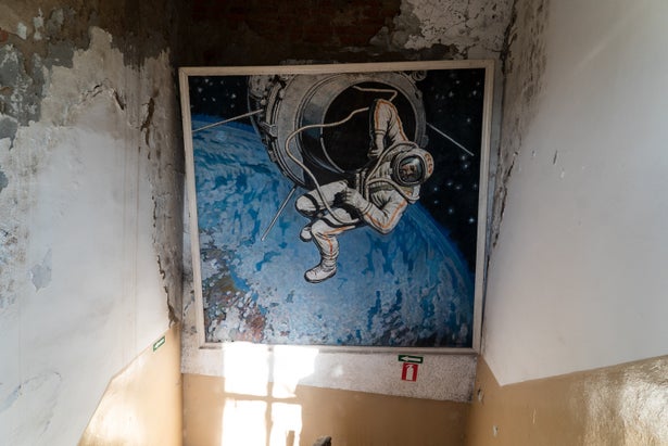 A mural of a cosmonaut outside a spacecraft in low-Earth orbit. The mural is on a wall inside a delapidated stairwell.