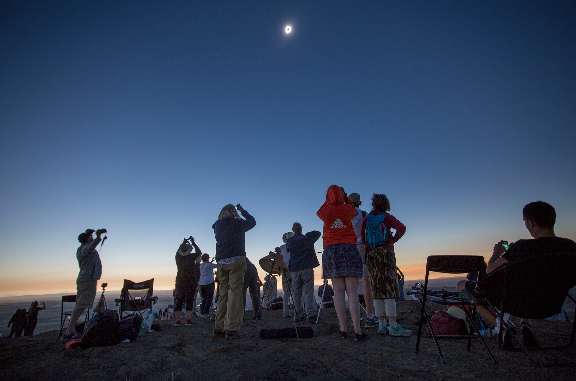 People gathered, standing as they watch a solar eclipse during totality.