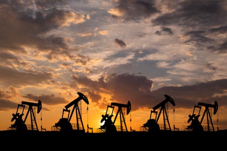 Five oil derricks silhouetted against the setting sun and a cloudy sky
