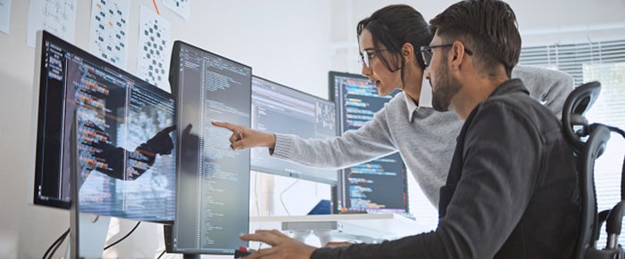 A man seated looking at a computer screen and a woman standing, point at the screen