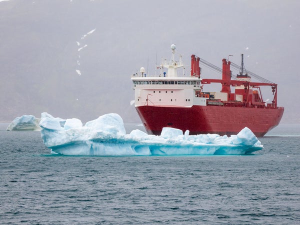 Iceberg drifts in front of red container ship