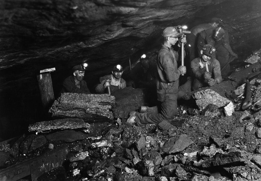 Un grupo de mineros de carbón, algunos que usan mierda, todos con cascos equipados con lámparas de mineros, en una mina de carbón, Estados Unidos, alrededor de 1935