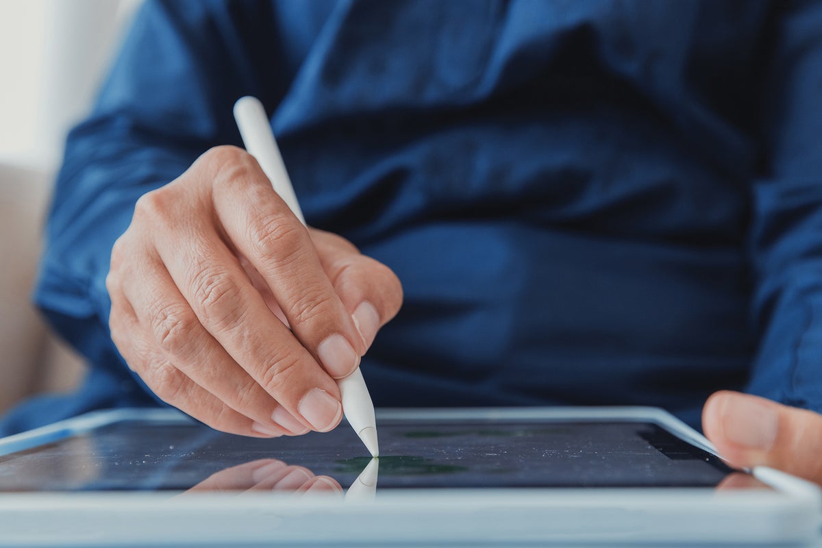 A hand holding a stylus above a tablet