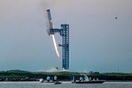 Starship's Super Heavy Booster is grappled at the launch pad in Starbase near Boca Chica, Texas as onlookers watch from boats in the water nearby