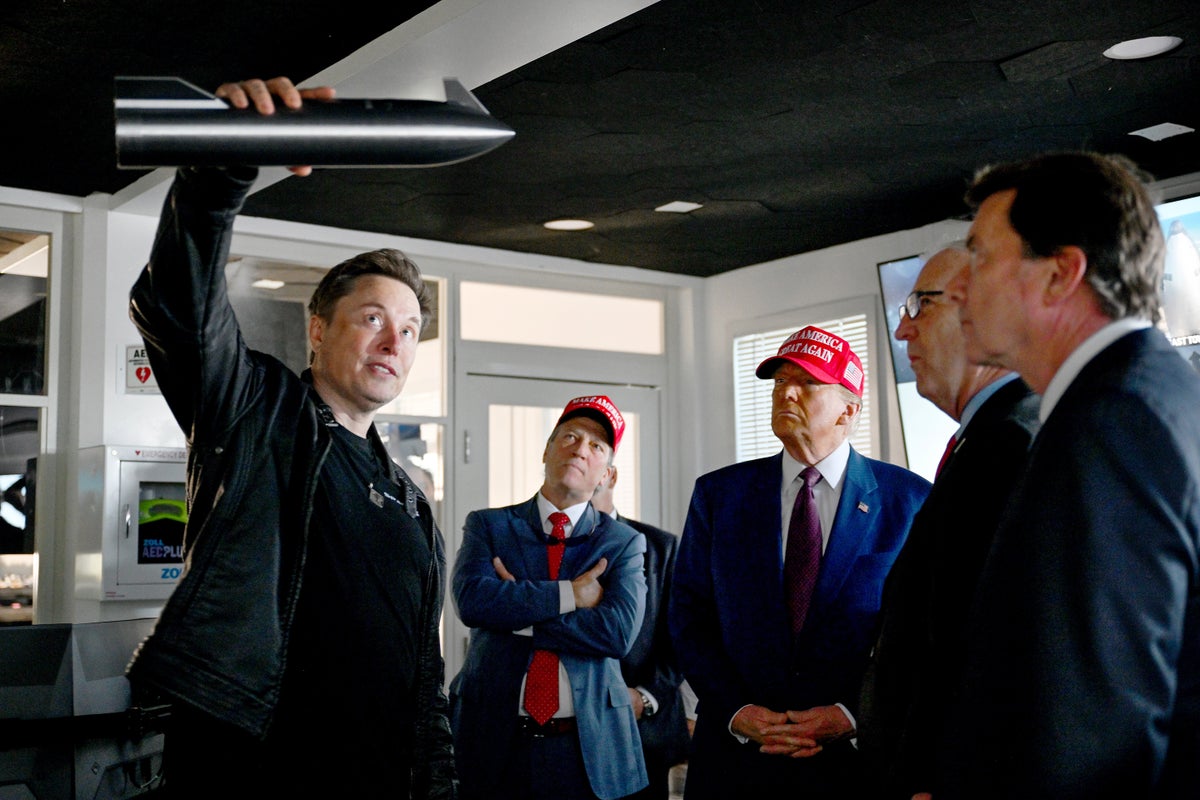 Elon Musk holds up a miniature model of SpaceX's Starship as Donald Trump and other visitors look on