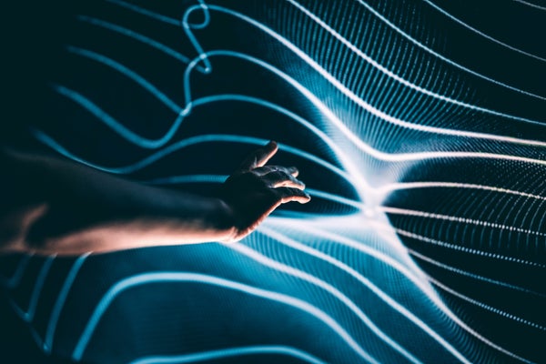 يد بشرية ممدودة نحو سطح متموج ومرقش بالضوء من الخطوط المتشابكة المجردة