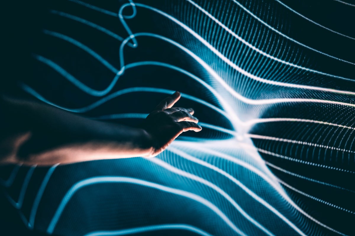 A human hand outstretched towards a rippling, light-dappled surface of abstract interwoven lines