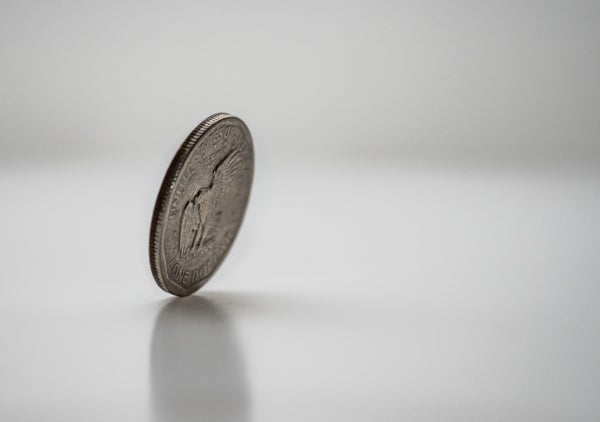 A quarter balances on its edge, tilted forward as if it's about to drop.