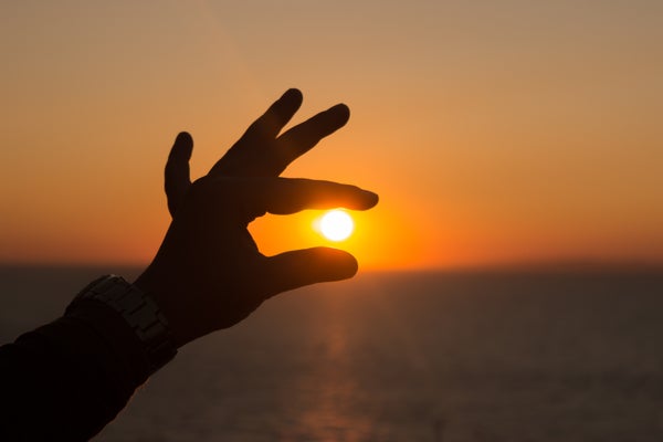 A person holding their hand up in front of the sky at dusk to create the illusion that they are grabbing the sun with their fingers