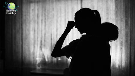 A silhouette of a woman holding her head with one hand and a child in her other arm in black and white