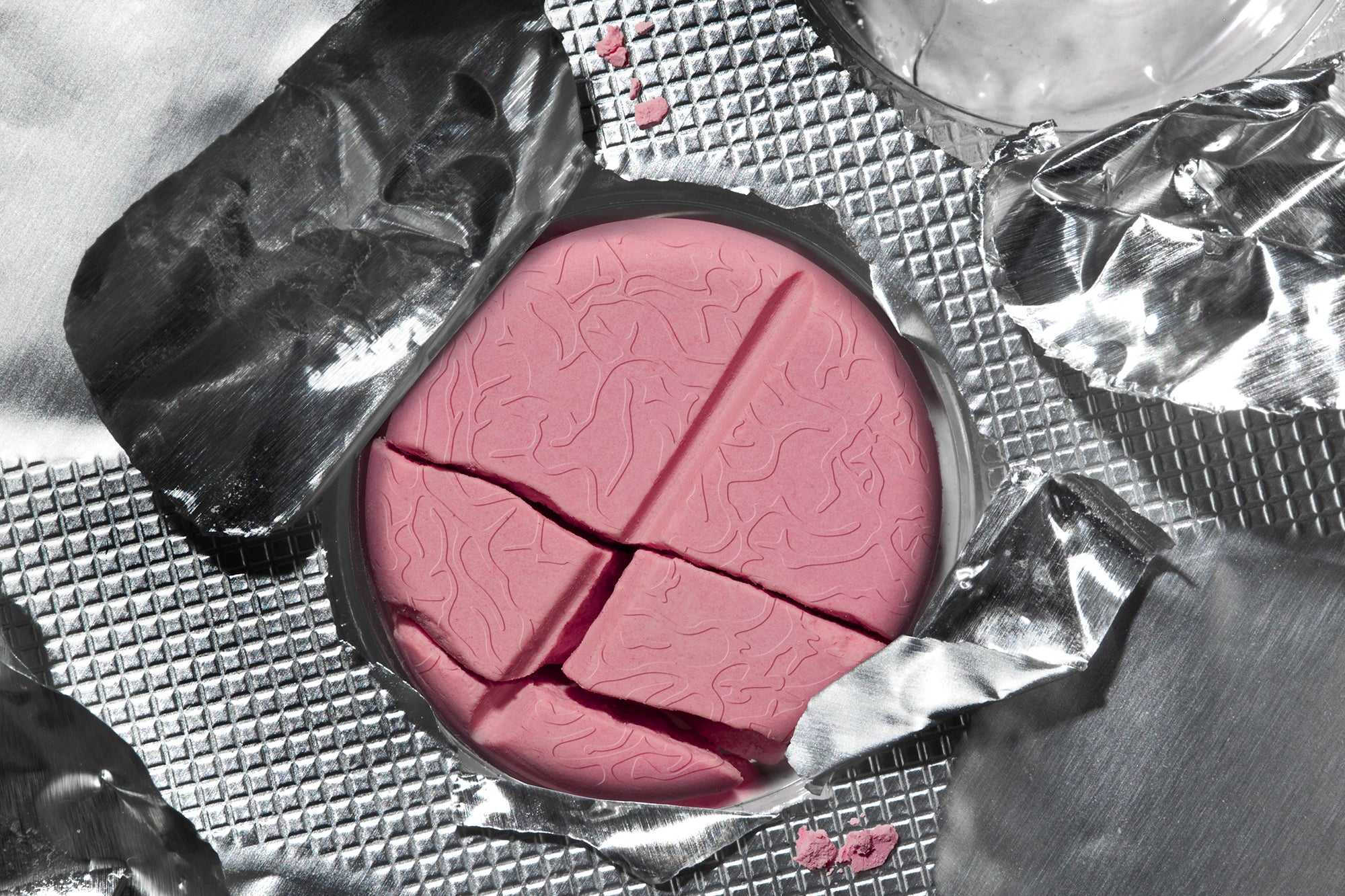 An open blister pack with a round pink broken tablet pill inside. The pill has subtle texture resembling an illustration depicting folds of the brain