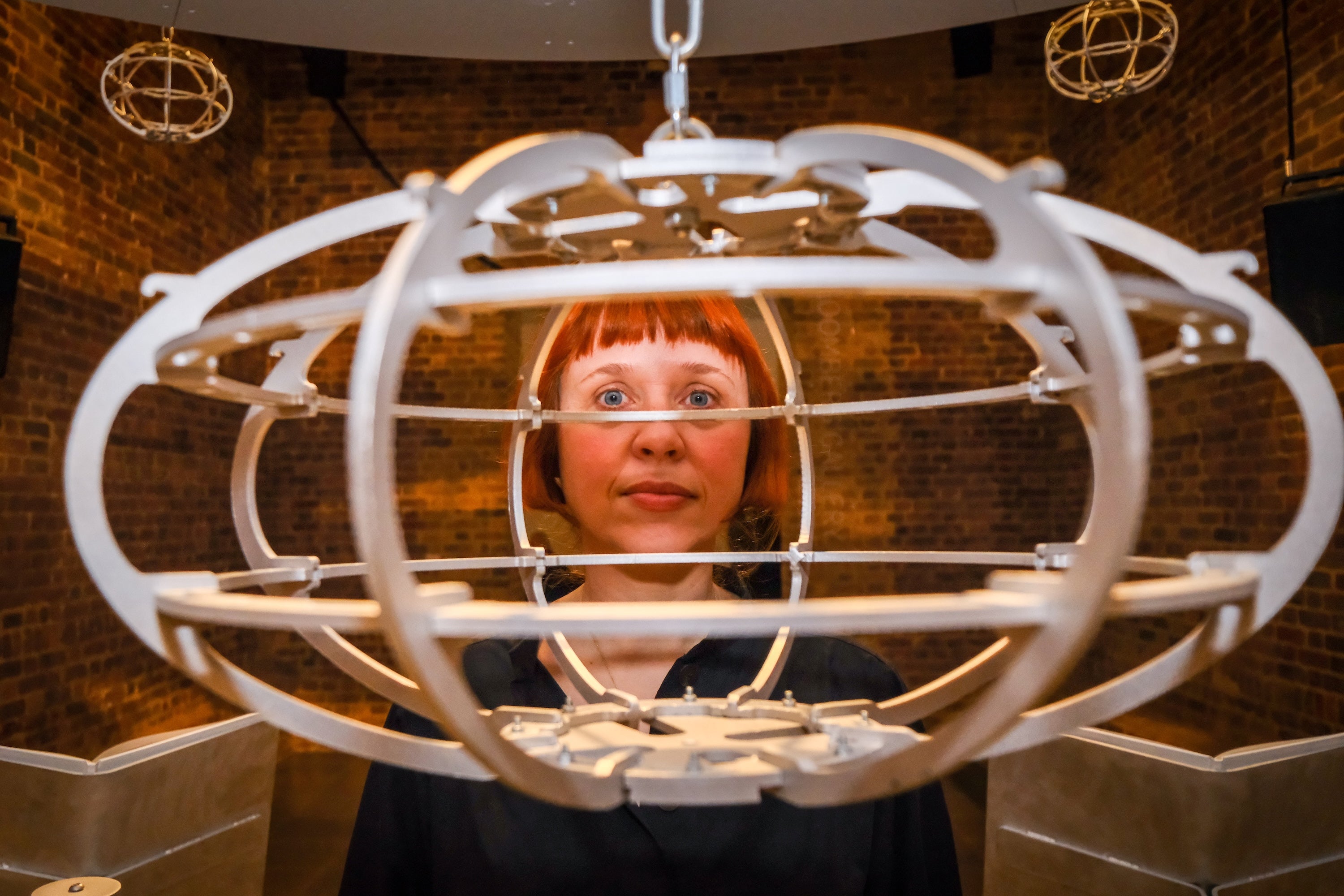 Holly Herndon standing indoors at Serpentine North Gallery in London, framed by a suspended circular sculptural structure, with brick walls in the background.