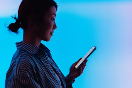 Side view of woman in silhouette using smartphone against illuminated blue screen