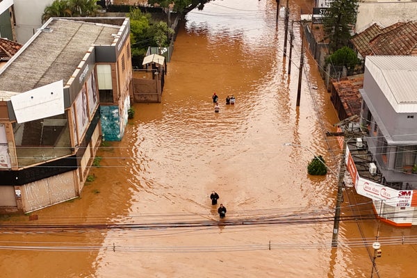 Aerial view of men wading through flooded street with brown water lined with stores on both sides