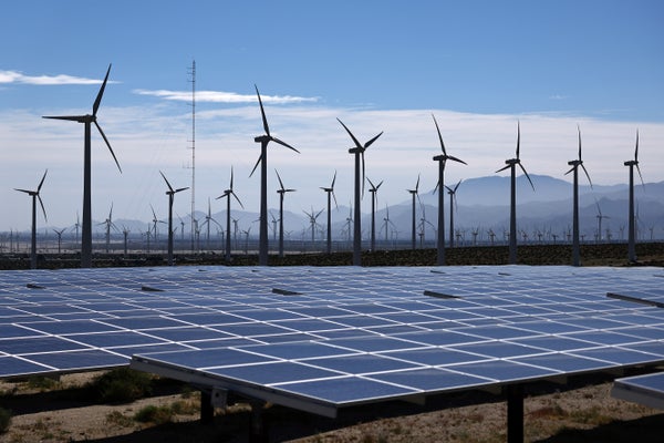 Wind turbined behind solar panels in landscape.