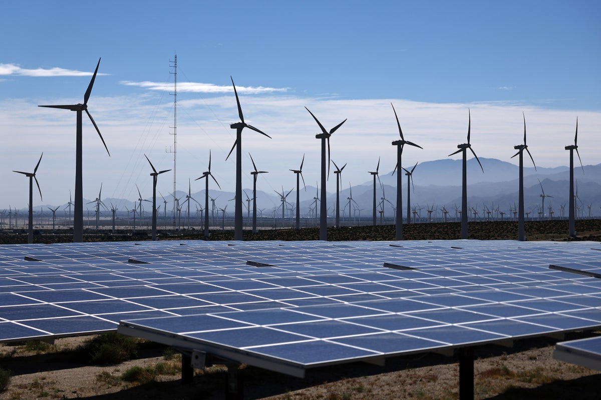 Wind turbined behind solar panels in landscape.