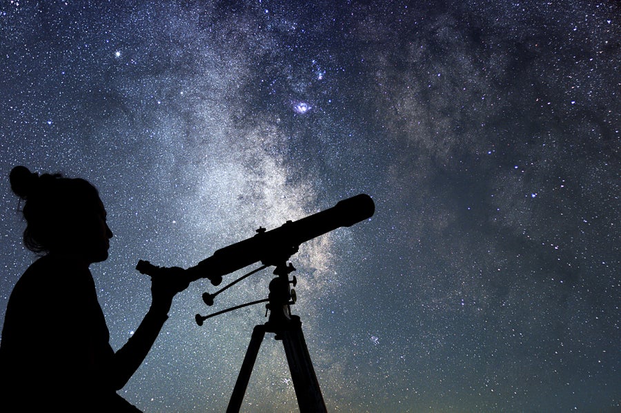 Silhouette of a woman with telescope beneath a starry sky