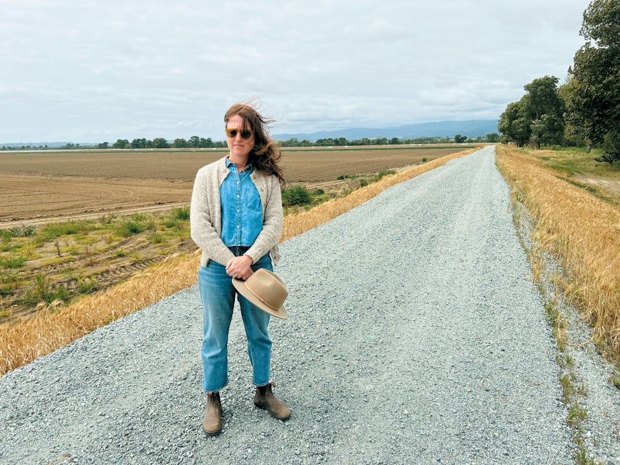 A woman with long hair standing on a road open field in background