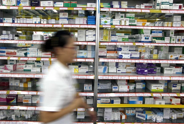 A blurry female pharmacist walking past a shelf with medicine.