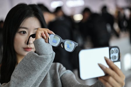 This picture taken on November 13, 2025 shows a woman checking a pair of Rokid glasses with display and camera using artificial intelligence (AI) and augmented reality (AR) during a presentation event in Hangzhou, in China's eastern Zhejiang province. In China, AI glasses let the wearer pay in shops with just a glance at a QR code and a voice command, as a growing number of companies look to conquer both growing domestic and overseas markets. Interest in smart eyewear is soaring worldwide after more than a decade of stalled promise, with advances in artificial intelligence sparking renewed interest in the sector. (Photo by Hector RETAMAL / AFP via Getty Images)