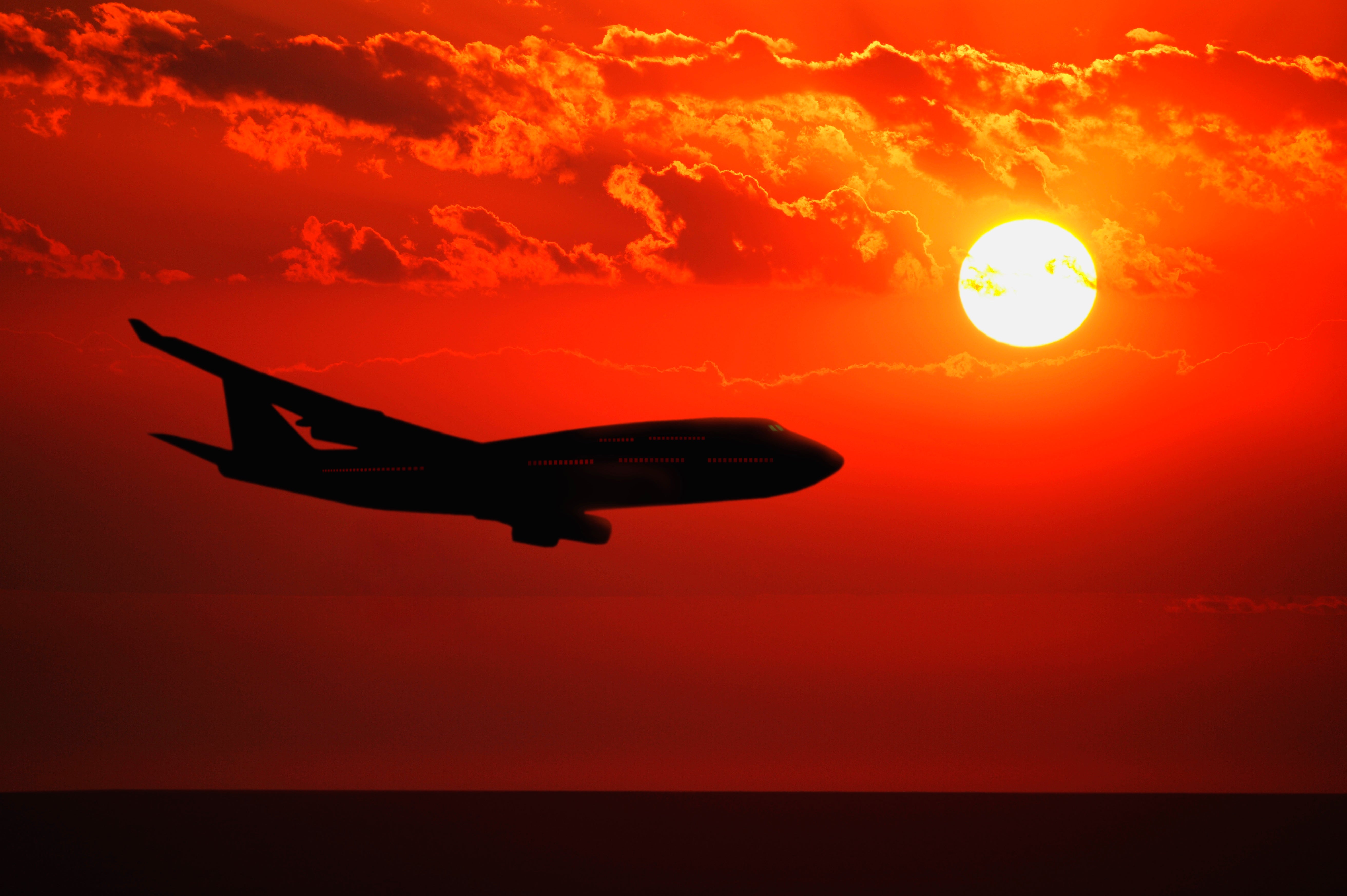 Plane flying against a red/orange sky and sun