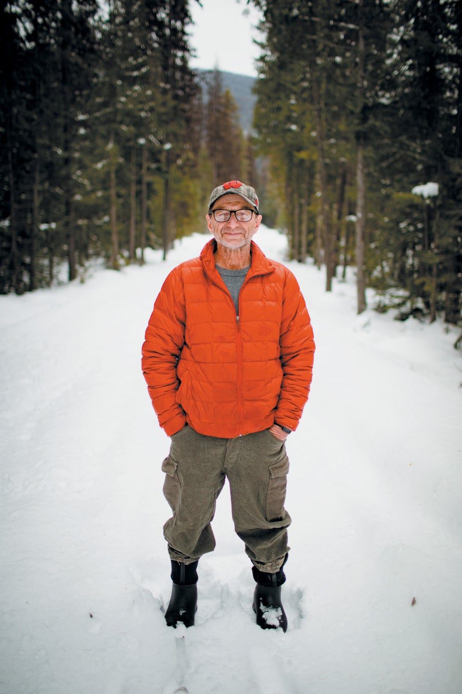 Photo of Rick Bass wearing an orange coat in front of a snowy forest.