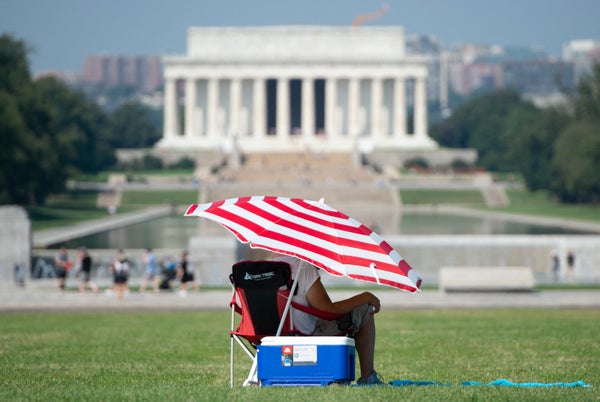 View of the Lincoln Memorial with a person sitting under a red and white striped umbrella with a blue cooler in the foreground.