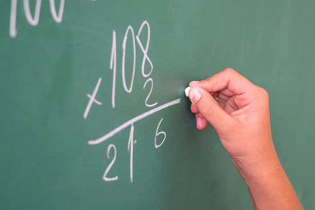 A person with chalk at a blackboard solves a math problem
