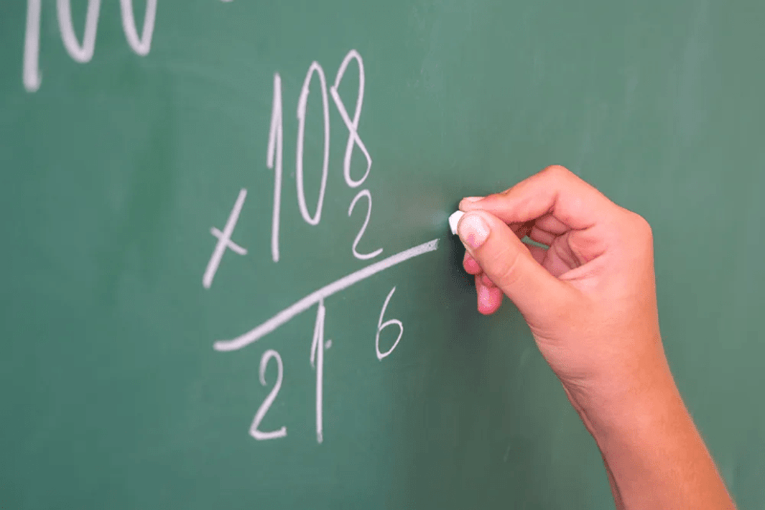 A person with chalk at a blackboard solves a math problem