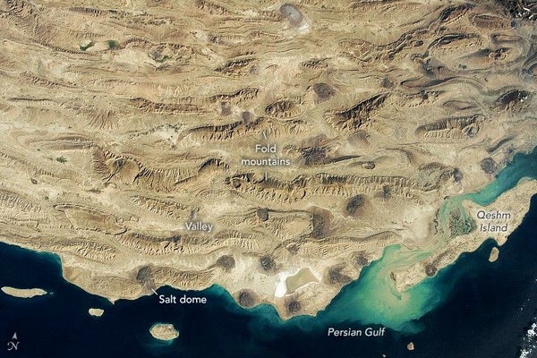 Las tres cuartas partes superiores de la imagen son un terreno montañoso de color beige y marrón con el azul profundo del Golfo Pérsico en la parte inferior de la foto.