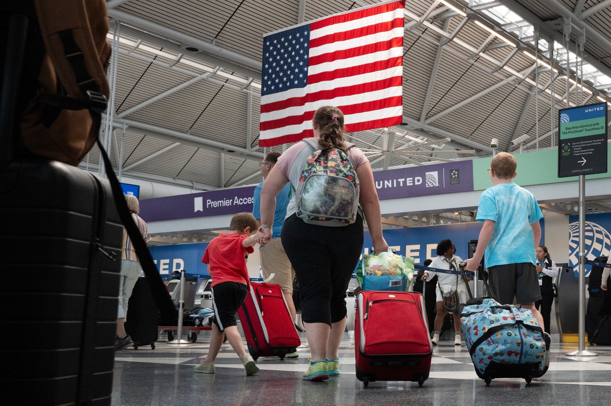 Passengers walk through an airport pulling suitcases with an American flag hanging from the ceiling