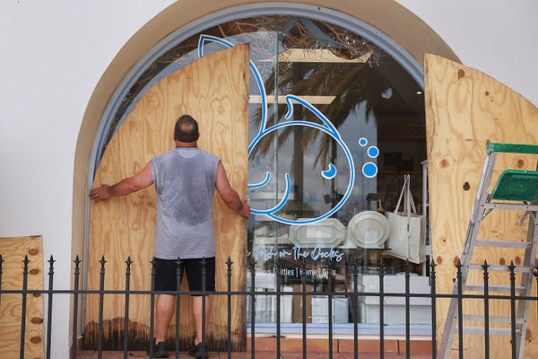 A man places plywood over an arched window on the storefront for a fish store in Florida