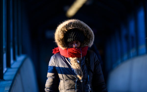 A woman walks on a pedestrian bridge with her face covered to protect from the cold.