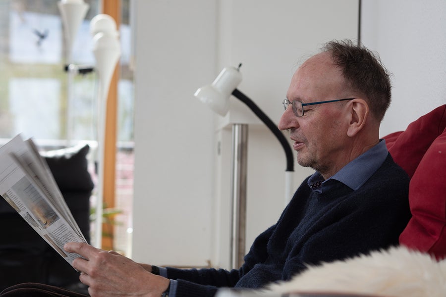 Profile picture of elderly man sitting on a sofa and reading a newspaper.
