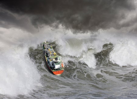 An oil tanker ship churns up a huge tsunami like wave in rough seas.