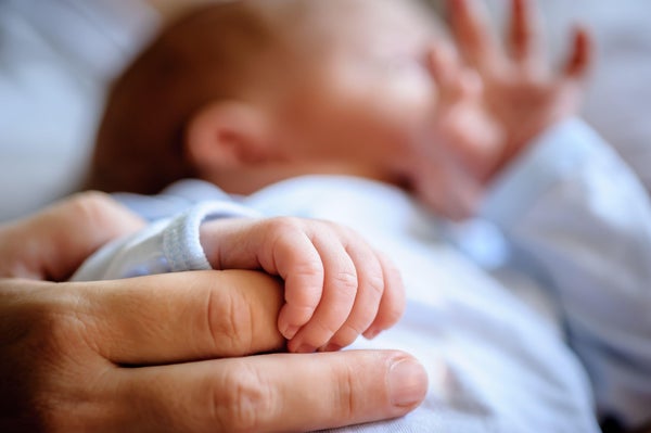 Close-up detail macro view of baby holding on to mom's finger with his little hand.