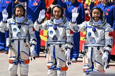 Three astronauts pause and wave in a large crowd