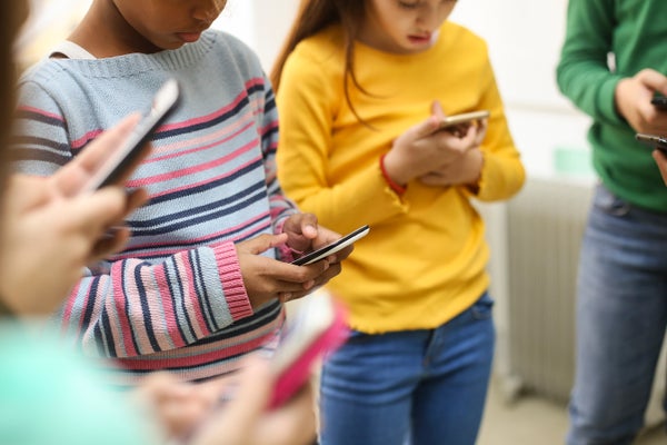 Group of children, about 9-10 years old and multi-ethnic, standing together while using smart phones at school