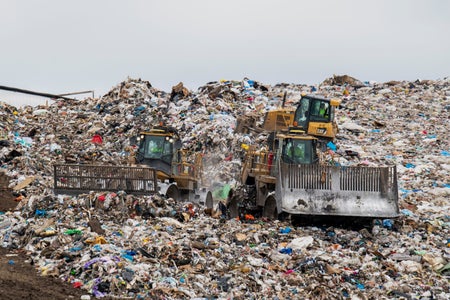 Two garbage trucks moving trash at a landfill.