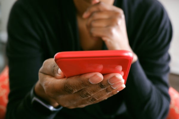 Unrecognizable black woman uses smart phone while sitting in chair in living room