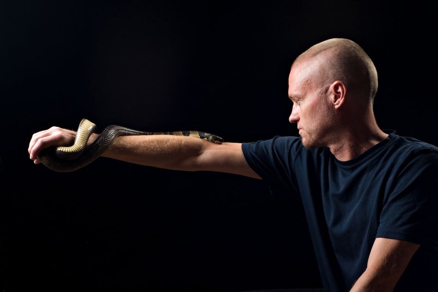 Man holding snake on arm against a black background