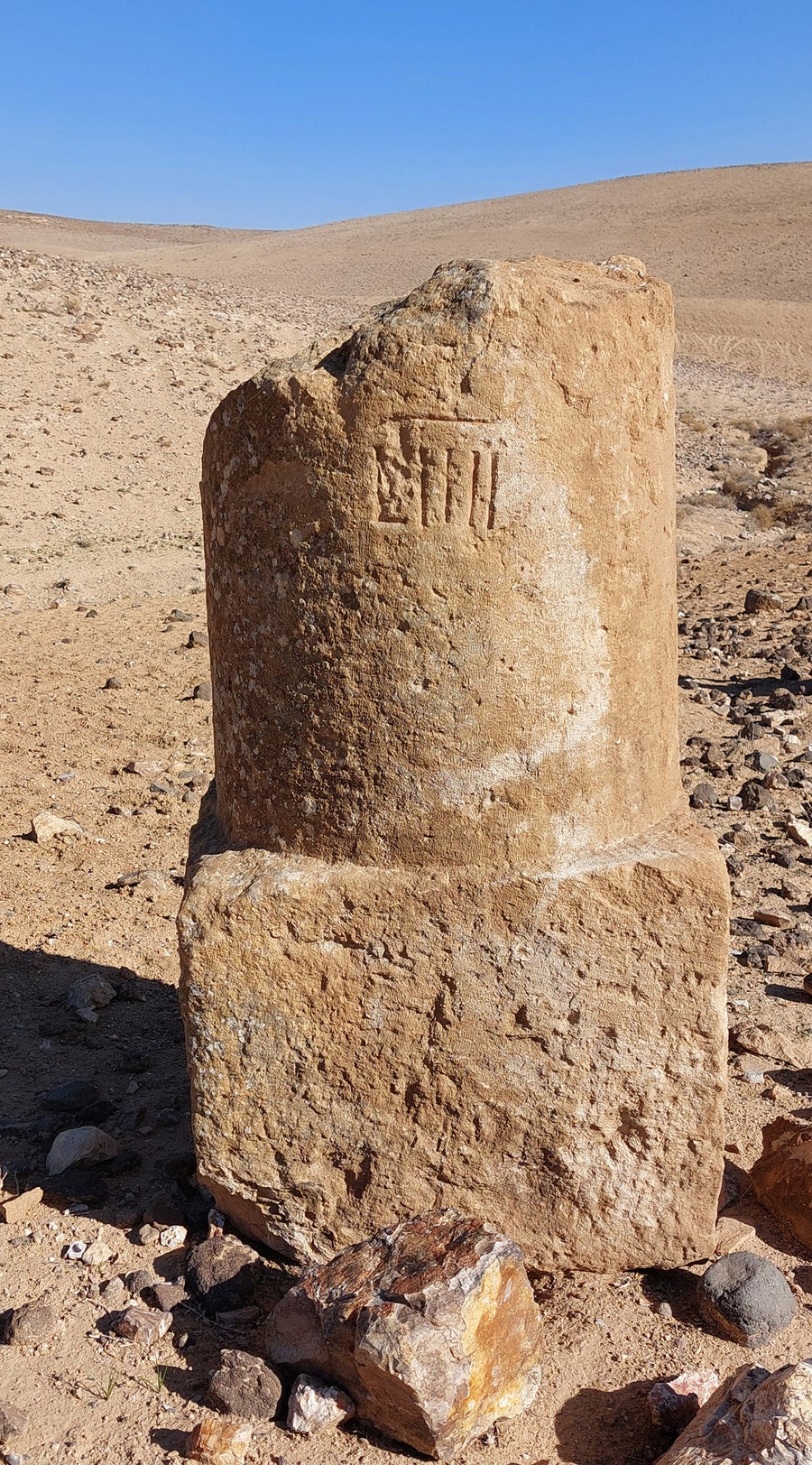 A tan-colored pillar base with a broken-off top, with a desert view in the background