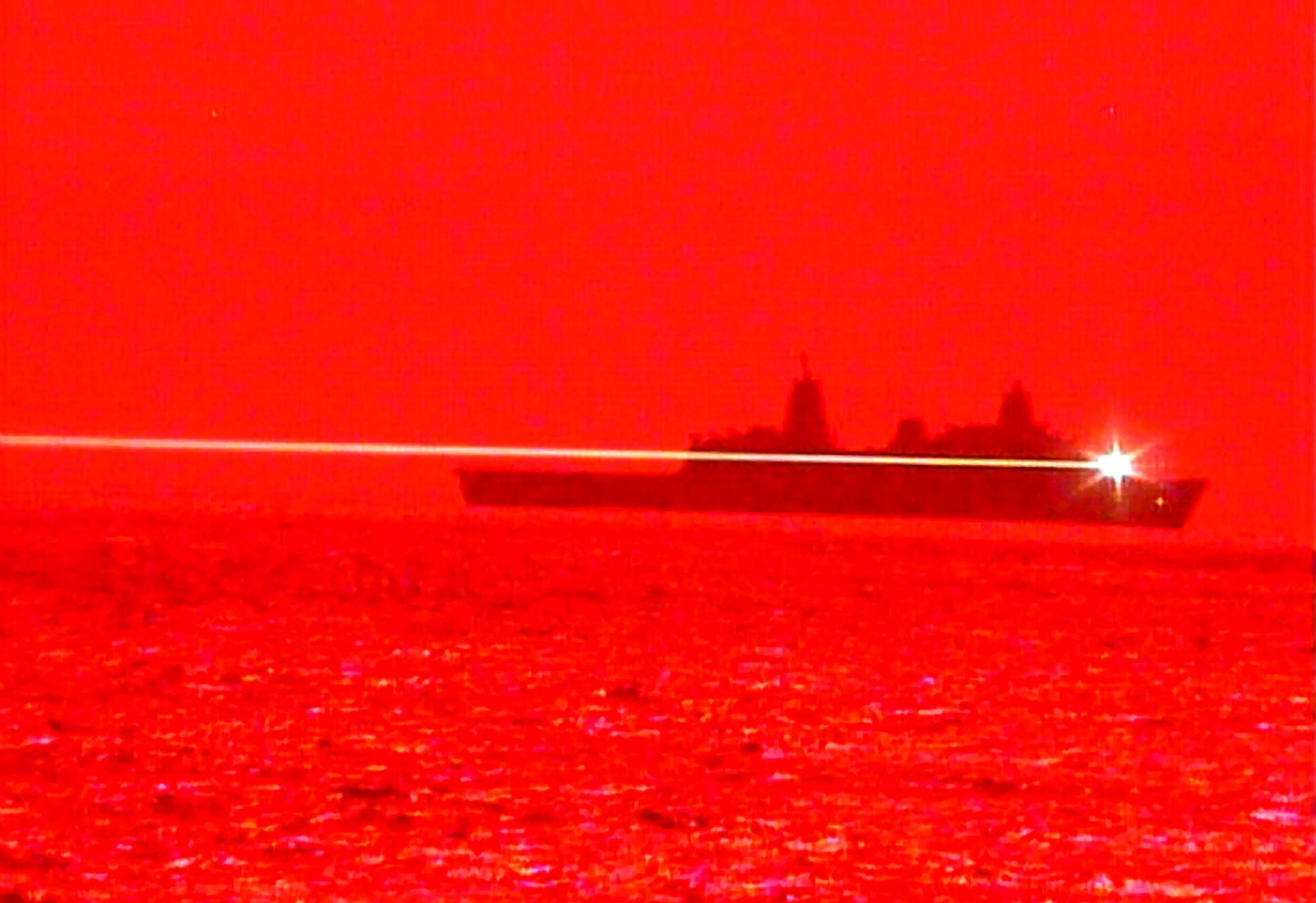 Monochromatic red image showing ship at sea with a laser shooting across frame