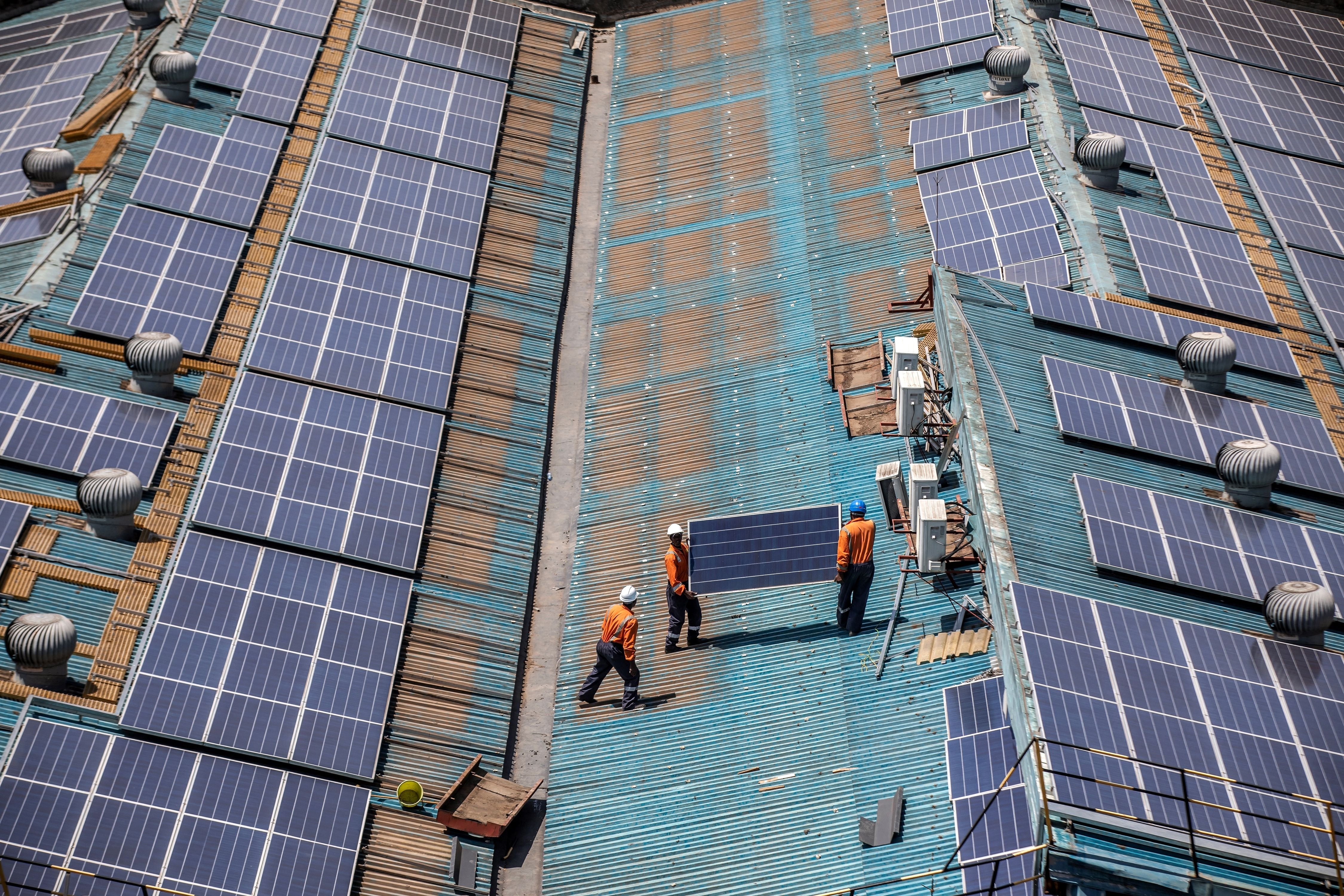 Technicians in orange gear install solar panels on a large rooftop.