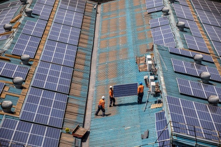 Technicians in orange gear install solar panels on a large rooftop.