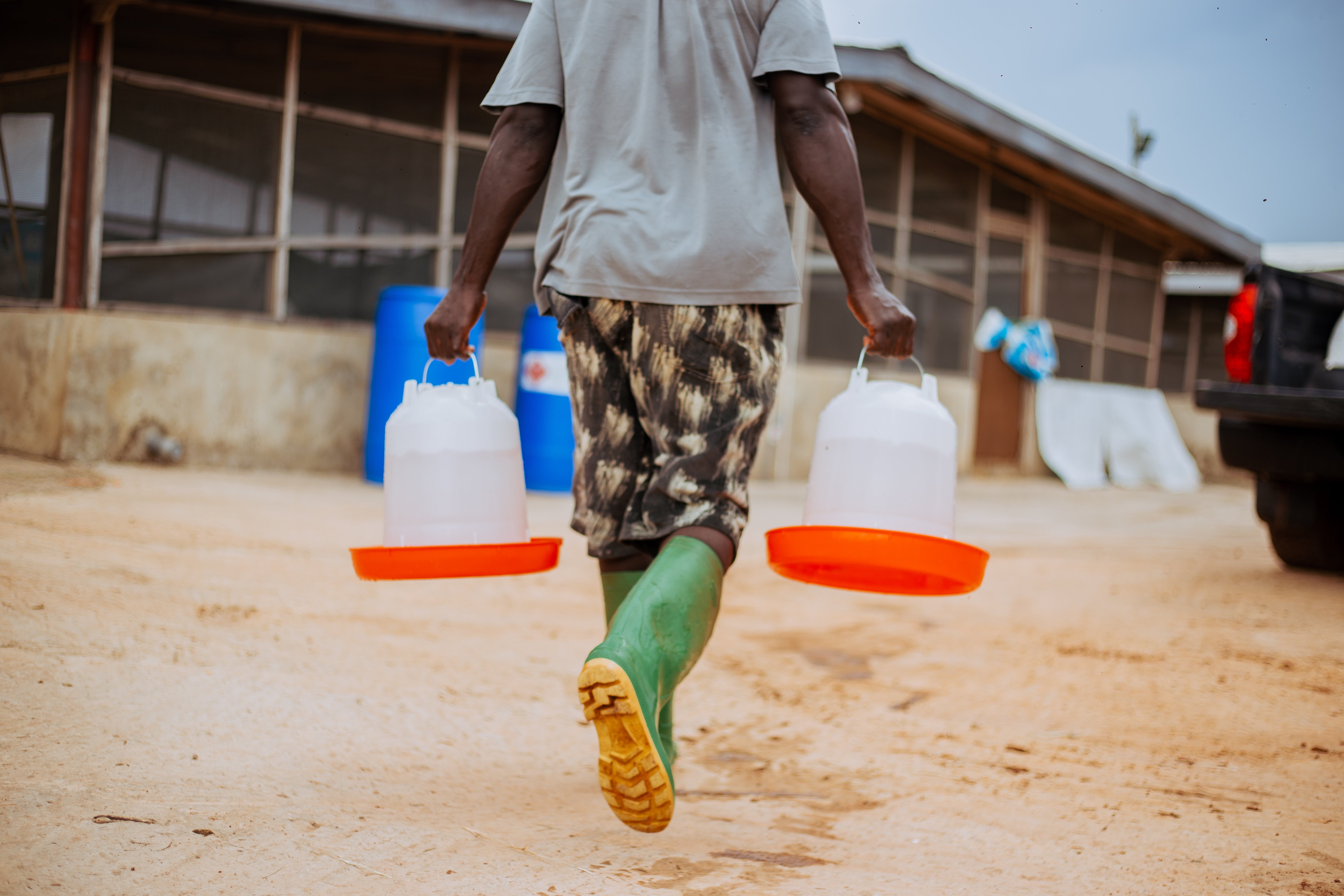 Man with green boots and water containers on a deserted dirt road.