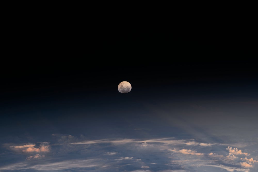 Fotografía capturada desde la Estación Espacial Internacional que muestra la luna de la Tierra sobre las nubes con las espectaculares sombras de una puesta de sol. La luz de la Luna es refractada por la atmósfera terrestre dándole una apariencia esferoide.