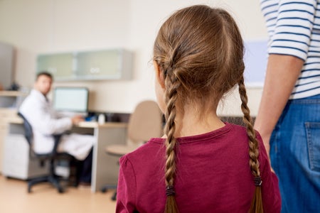 Scared little girl with red shirt and braids entering doctors office with Mom.