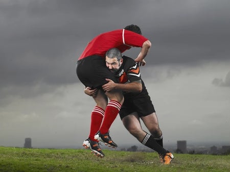 Two rugby players getting physical, against a gray sky.